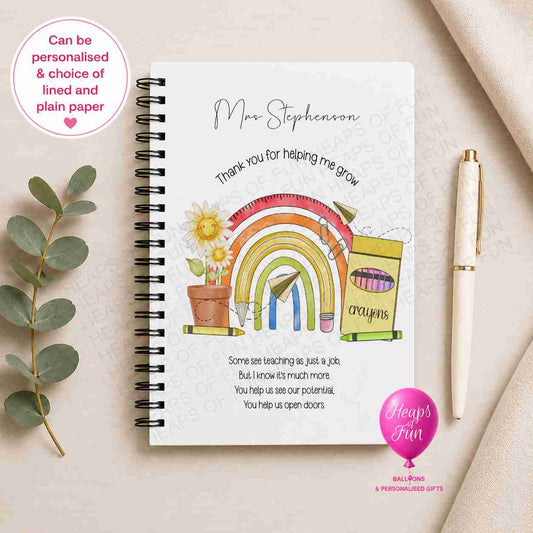 Personalised spiral-bound teacher notebook featuring a colourful rainbow, flowers, crayons, and "Thank You for Helping Me Grow" design, customised with the teacher's name and available with lined or plain pages.
